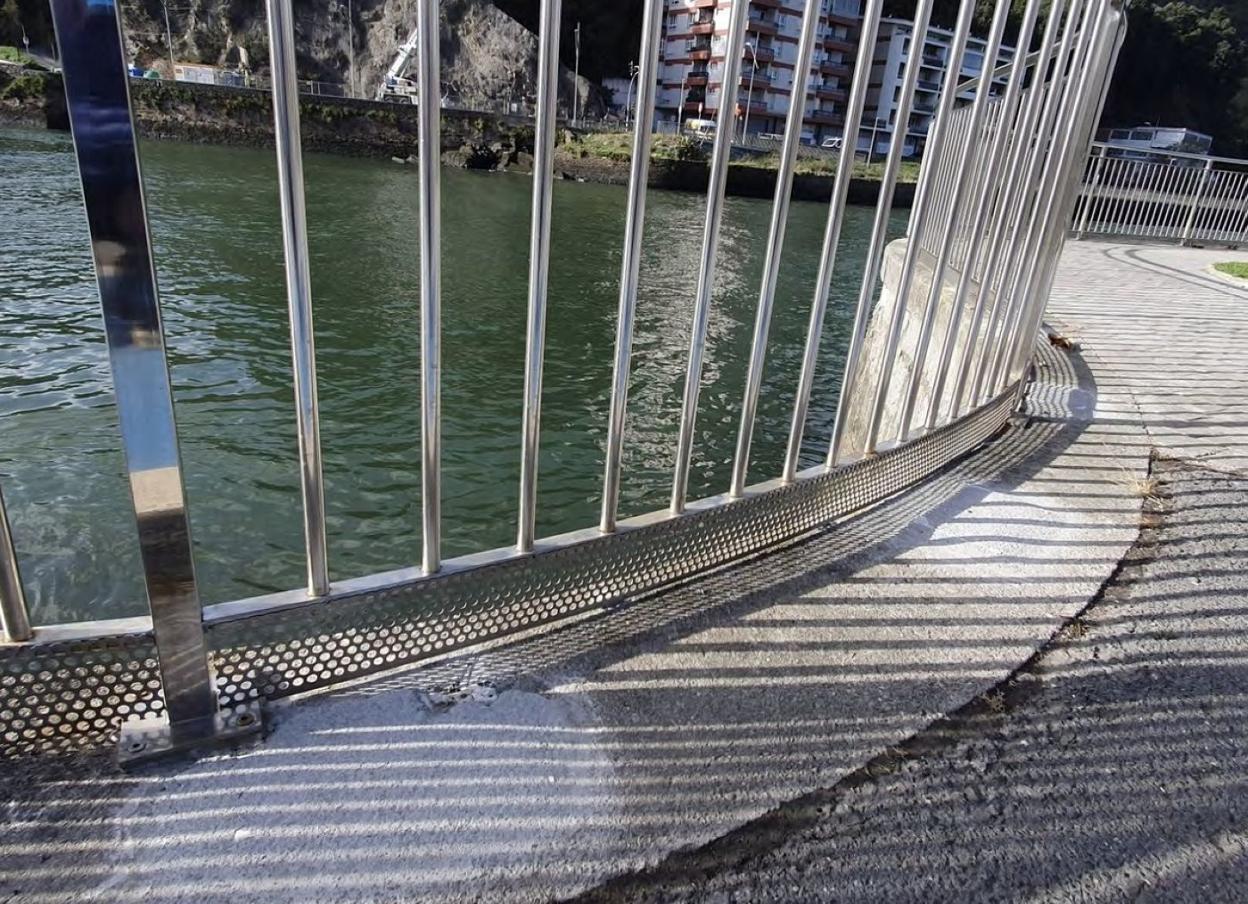 Rejilla protectora al pie de la barandilla instalada junto a la ría en Deba que evita la caída de basura. 