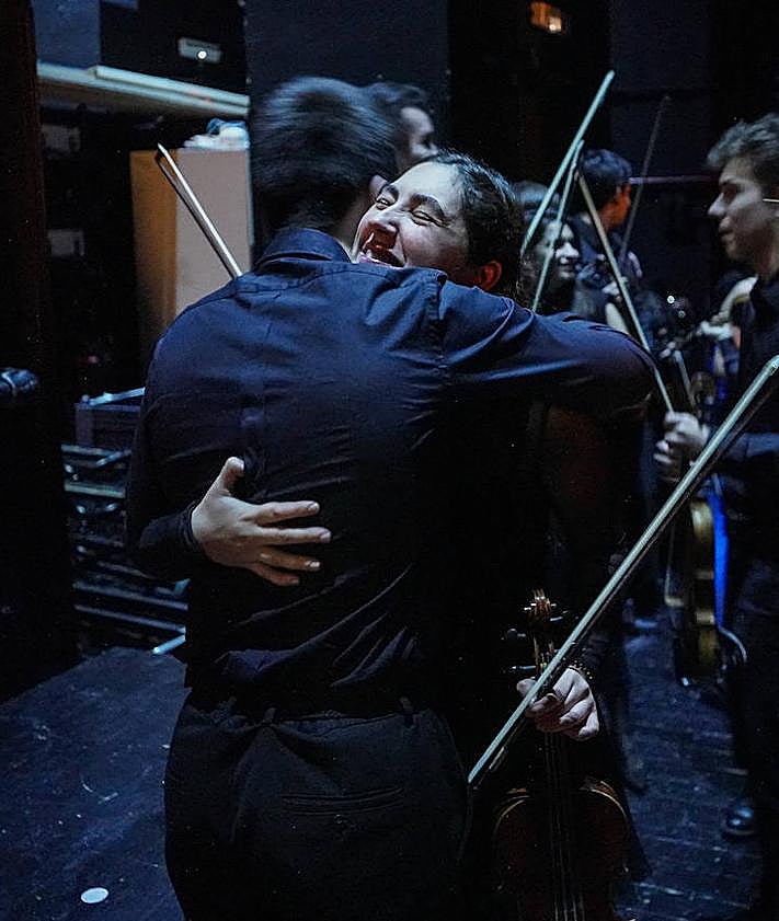 Imagen secundaria 2 - Los protagonistas no quisieron dejar pasar la oportunidad de inmortalizarse con el anfiteatro de fondo, antes de un concierto en el que muchos de ellos se estrenaban. La sección de vientos atiende a las explicaciones del director durante el ensayo general en el teatro donostiarra. Bromas, risas y abrazos al caer el telón.