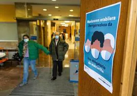 Dos pacientes abandonan el área de consultas externas del Hospital Donostia frente a un cartel que avisa de la obligatoriedad de portar la mascarilla.
