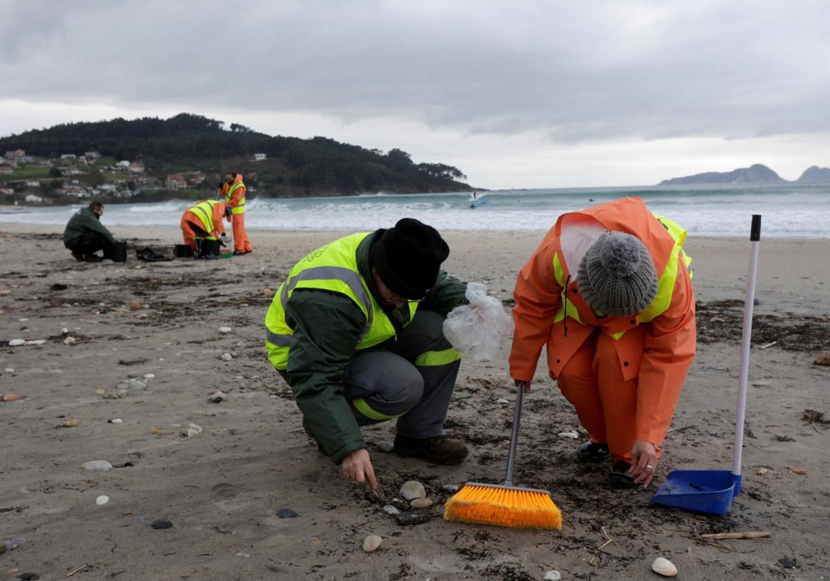 Dos personas recogen pélets en una de las playas de la localidad gallega de Nigrán.