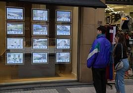 Dos jóvenes consultan los anuncios de alquiler en el escaparate de una agencia inmobiliaria.