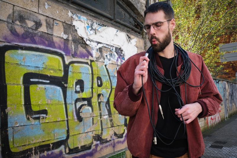 Asier, a medio camino entre el Antiguo y Jai Alai, con un cable de audio, imprescindible en sus grabaciones caseras, enrollado al cuello.