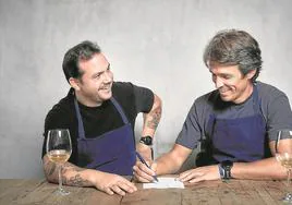 Nino Redruello escribe una receta ante la mirada sonriente del cocinero Manuel Villalba.