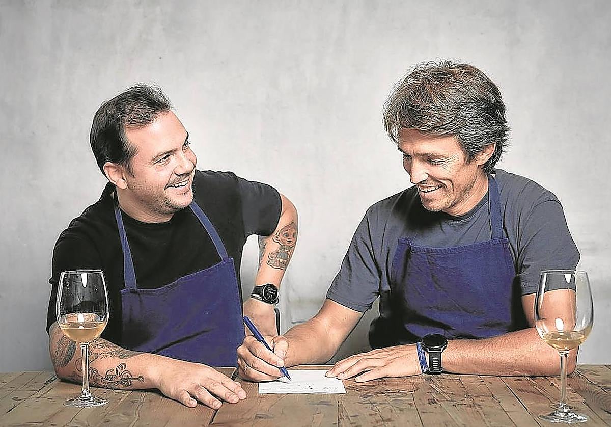 Nino Redruello escribe una receta ante la mirada sonriente del cocinero Manuel Villalba.