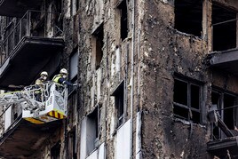 Bomberos subidos a una grúa sanean la ventana de una de las viviendas calcinadas por el fuego en Valencia.