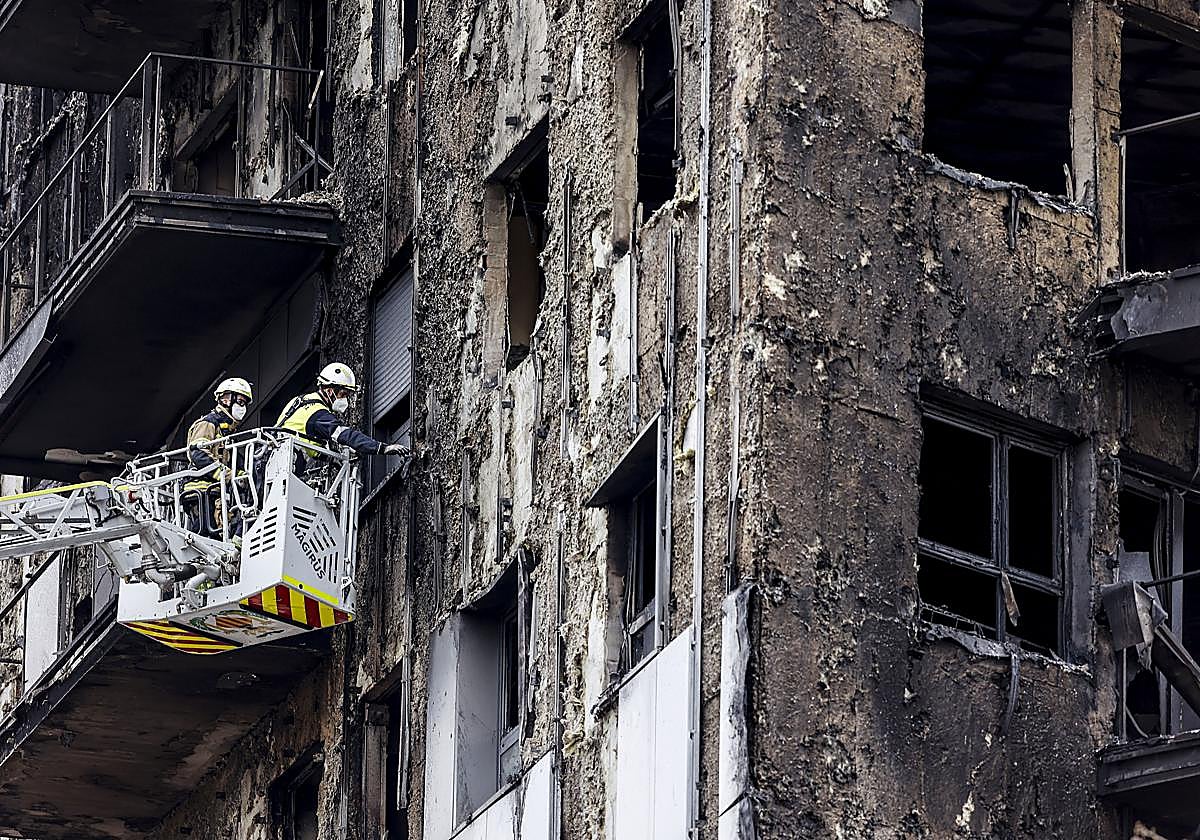 Bomberos subidos a una grúa sanean la ventana de una de las viviendas calcinadas por el fuego en Valencia.