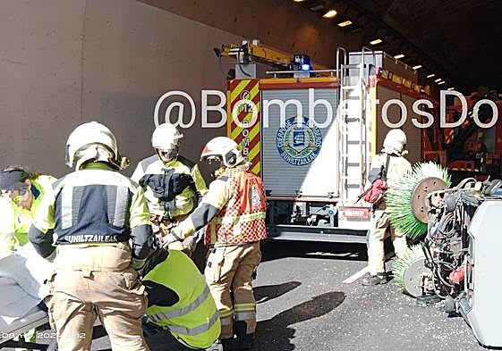 Personal sanitario y bomberos en el lugar del accidente, en el que se aprecia la barredora volcada.