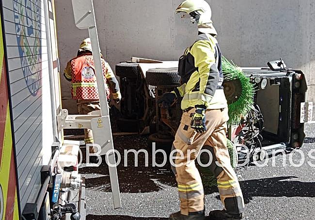 Los bomberos con el vehículo de limpieza volcado al fondo.
