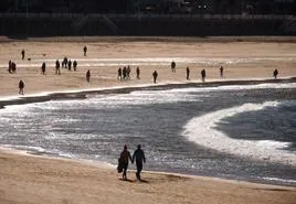 Una pareja camina de la mano por la orilla de la playa de La Concha