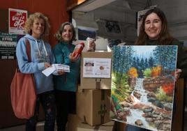 Dos ciudadanas posan con las rifas y paquetes de garbanzos en Elgoibar y una voluntaria muestra un cuadro donado por Gemma Monreal.