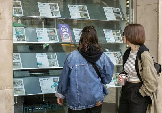 Dos jóvenes miran ofertas de vivienda en una inmobiliaria.