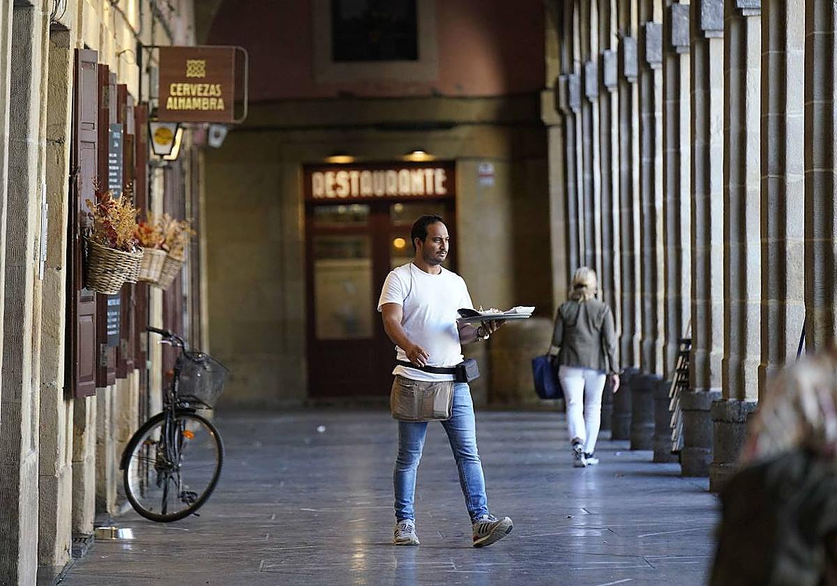 Un camarero se diriige a una mesa en la plaza de la Constitución de Donostia.