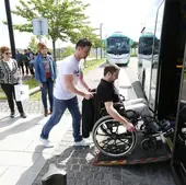 Una persona ayuda a otra con silla de ruedas a subir a un autobús.