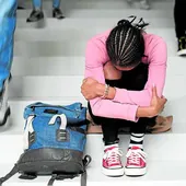 Una joven se tapa la cara sentada en las escaleras de un instituto.