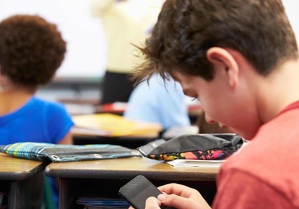 Un adolescente utiliza el móvil durante una clase.