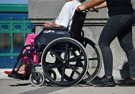 Una mujer dependiente pasea con su cuidadora por el puente de María Cristina.