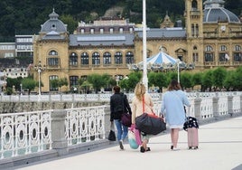 Tres turistas pasean con sus maletas por La Concha.