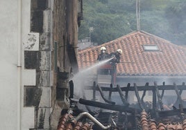 Dos bomberos apagan restos del fuego en una de las fachadas del portal número 6 de la calle Barrenkale de Mutriku.