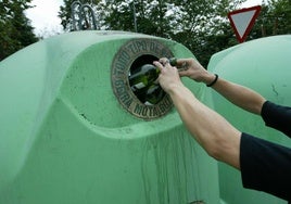 Una persona deposita varias botellas en un contenedor de vidrio.