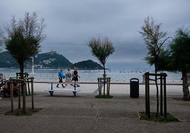 Tres hombres y una mujer caminan por el paseo de La Concha con el cielo nublado.
