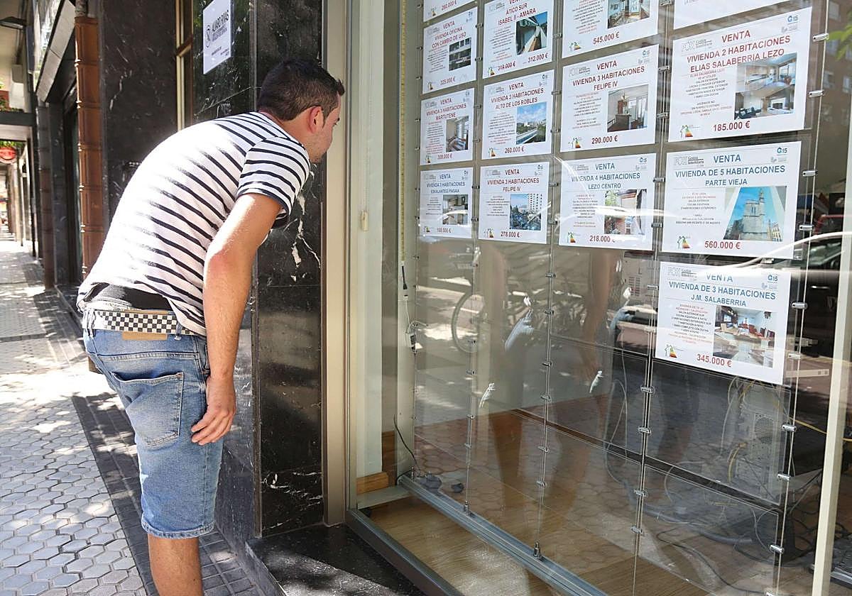 Un joven mira el escaparate de una inmobiliaria.