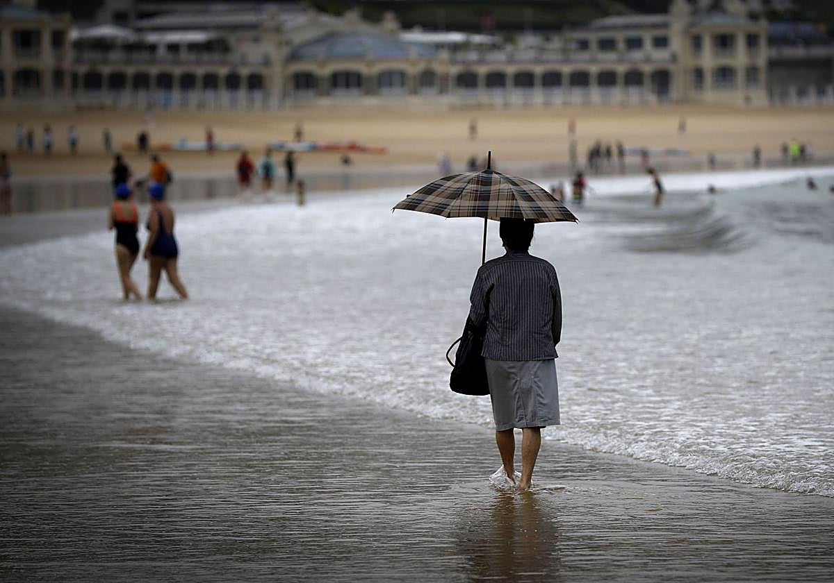 Una mujer pasea con un paragüas por la orilla de la playa de la Concha.