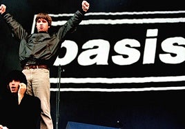Liam y Noel Gallagher con el icónico nombre de la banda de fondo durante un concierto en 1996.