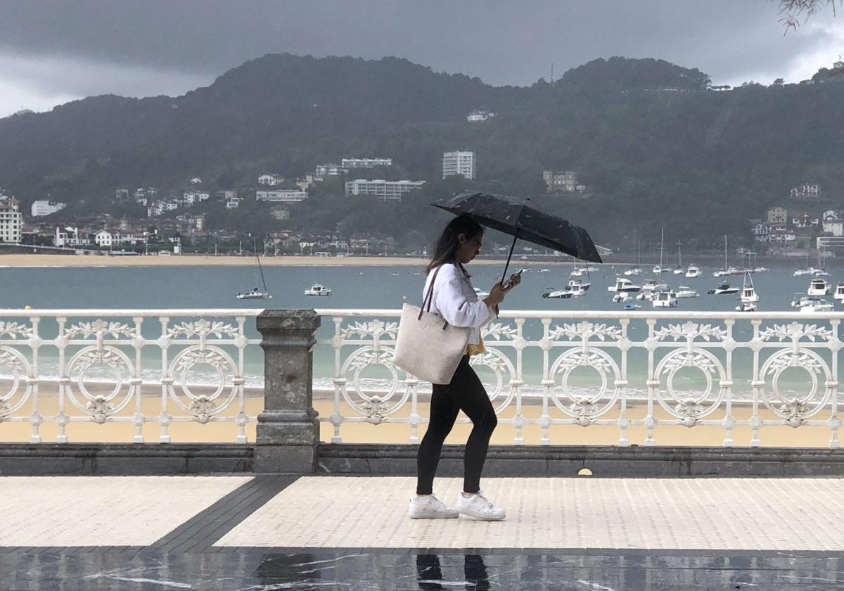 Una mujer se protege de la lluvia en La Concha