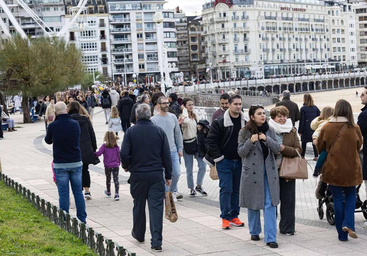 Diversas personas, algunas de ellas de origen extranejero, pasean junto a la playa de La Concha en San Sebastián.