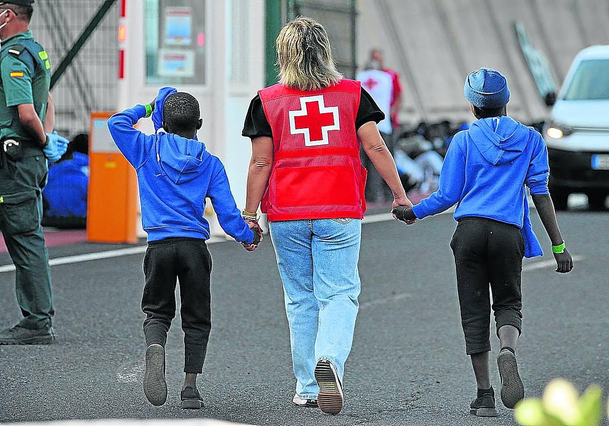 Una voluntaria de la Cruz Roja acompaña a dos menores extranjeros recién llegados a la isla de El Hierro, en Canarias