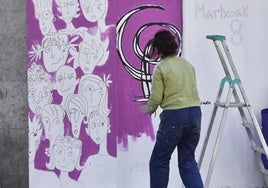 Una mujer pinta un mural en un rincón de la Parte Vieja.