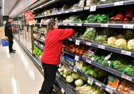 Una encargada se encarga de reponer la balda de hortalizas en un supermercado.