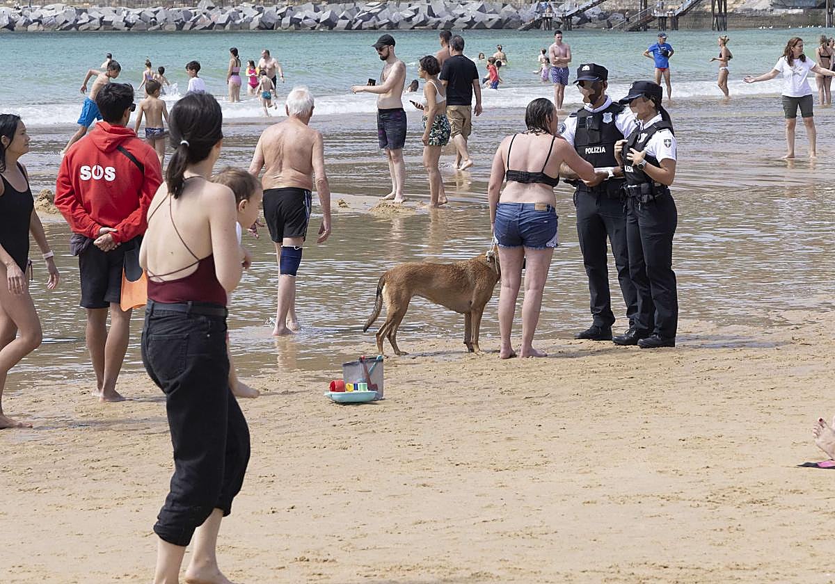 Dos agentes de la Guardia Municipal de San Sebastián charlan con la propietaria de un perro en la playa de La Concha.