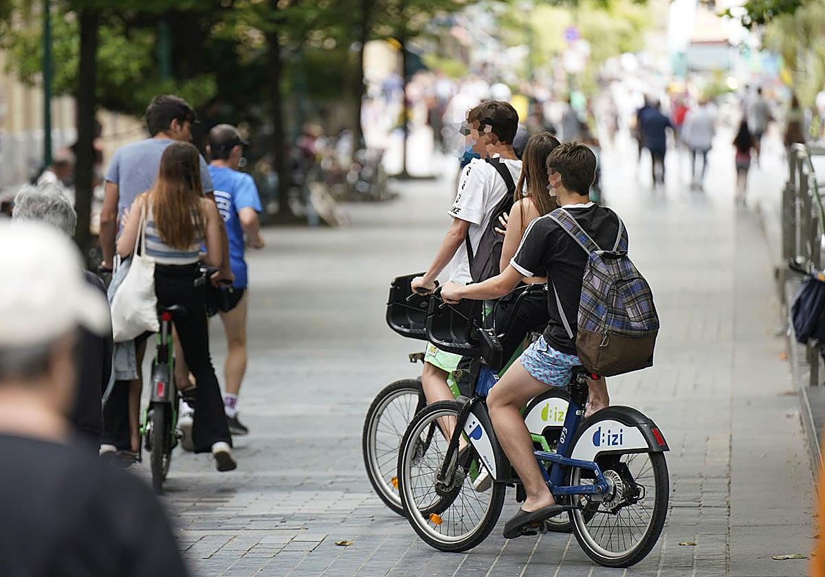 Varios jóvenes circulan en bicicleta por una acera del centro de San Sebastián.
