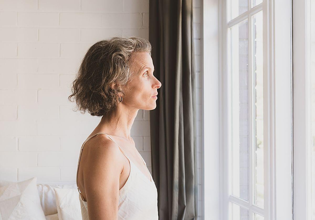 Una mujer mira a través de la ventana de un dormitorio.