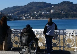 Una persona dependiente observa la bahía de La Concha junto a su cuidador.