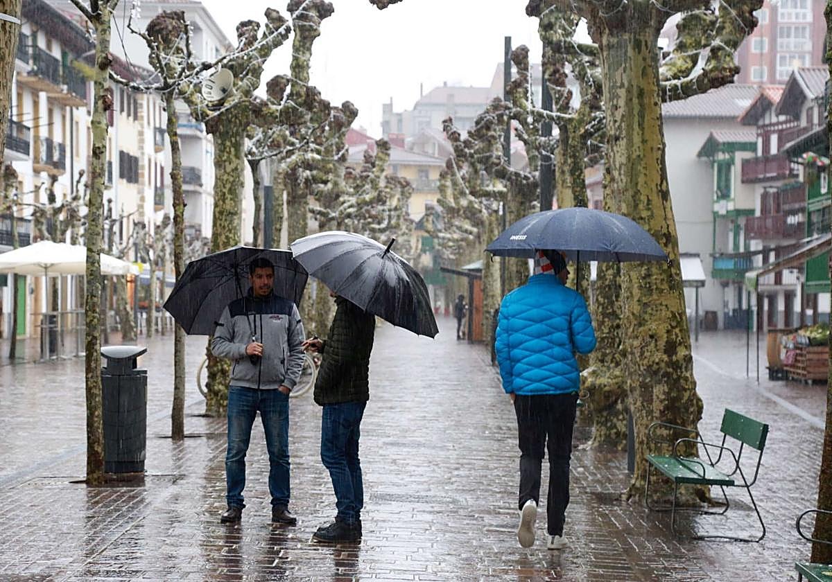 Varias personas caminan bajo el paraguas por la calle San Pedro de Hondarribia.