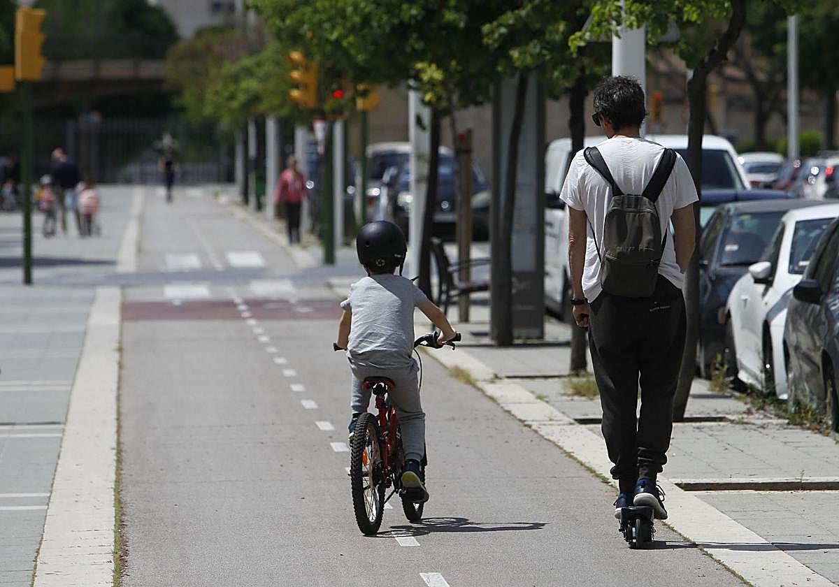 Un niño pasea en bicicleta junto a su padre, que va en patinete.