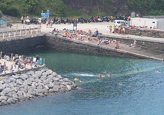 Numerosas personas disfrutan en torno a la vieja piscina de agua marina del puerto de Mutriku durante una jornada estival.