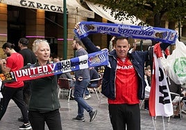 Dos aficionados del United muestran bufandas txuri-urdin y conmemorativas del duelo ante la Real Sociedad el 03 de noviembre de 2022