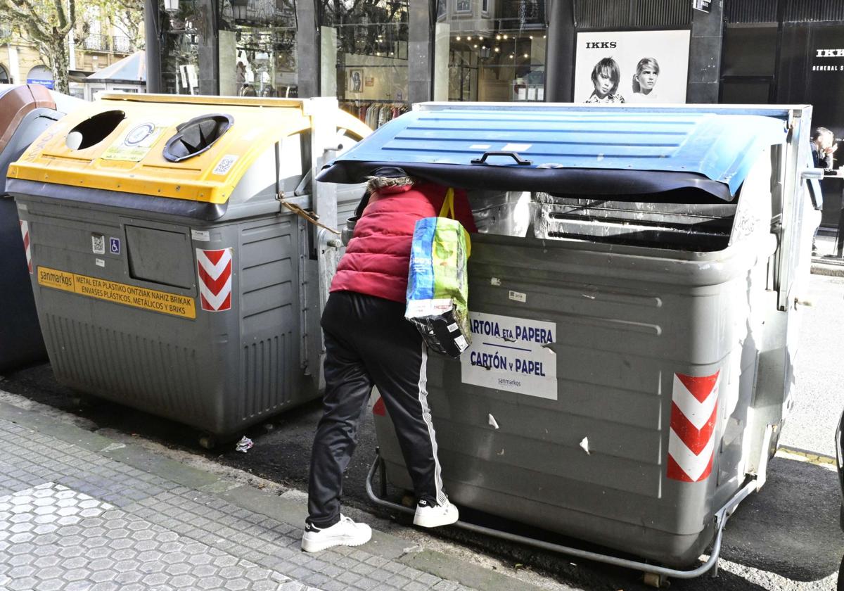 Una persona sin recursos rebusca en un contenedor de basura en Donostia.