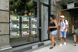 Una pareja observa el escaparate de una inmobiliaria de Donostia.