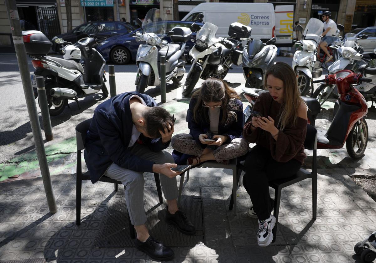 Varios jóvenes consultan sus móviles en una terraza.