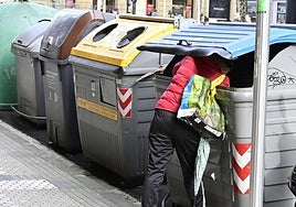 Una persona en situación de calle rebusca entre un contenedor de basura en Donostia.
