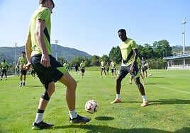 Dos jugadores se pasan el balón ante la mirada de sus compañeros en un entrenamiento en Zubieta.