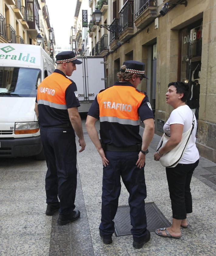 Imagen secundaria 2 - El bus turístico, atascado en el paseo Salamanca por culpa de una furgoneta que sobresale de la plaza de aparcamiento. Debajo, el agente Igor Ayerdi se baja del coche patrulla para felicitar un cumpleaños durante el confinamiento y dos agentes conversan con una mujer en la Parte Vieja en el primer día del cuerpo, en 2009. 