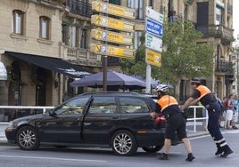 Dos agentes de Movilidad empujan un turismo averiado en la plaza Euskadi de Gros.