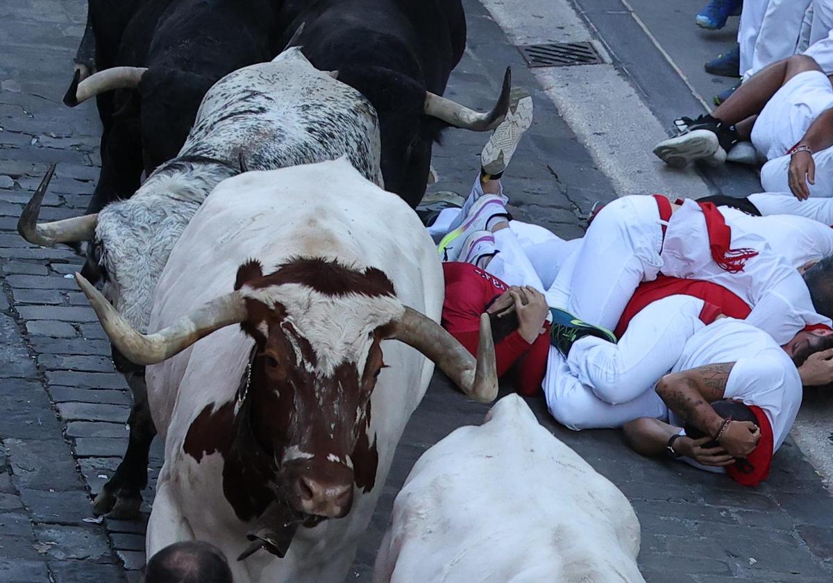 Varios corredores se protegen tras caer al paso de los toros de la ganadería Cebada Gago durante el segundo encierro de los Sanfermines este martes, en Pamplona.