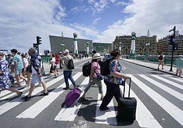 Dos turistas cruzan con sus maletas el puente del Kursaal.