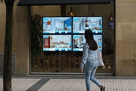 Una joven pasa ante el escaparate de una inmobiliaria en Donostia.